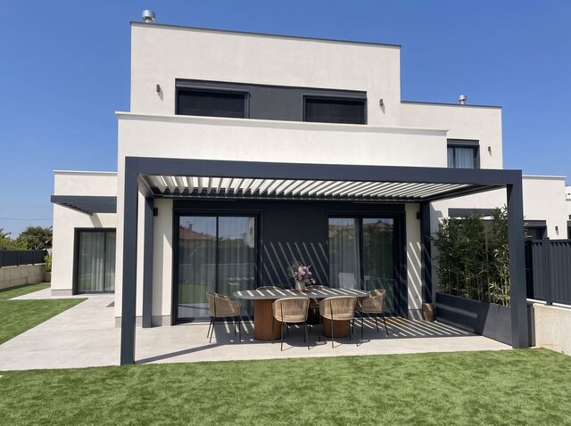 Pérgola de techo fijo CERCA adosada a la fachada de una vivienda, funcionando como porche